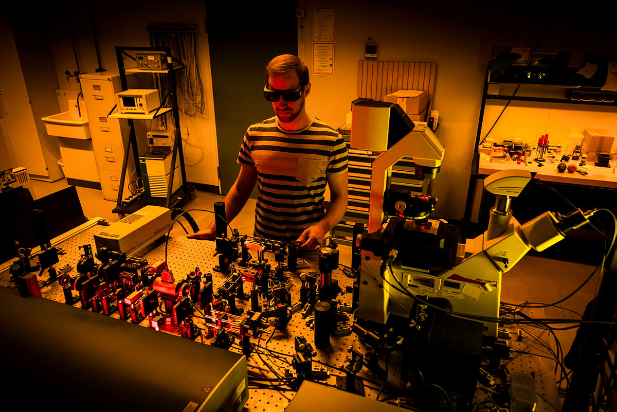 Ein Mann arbeitet mit Lasern im Labor, trägt Schutzbrille.